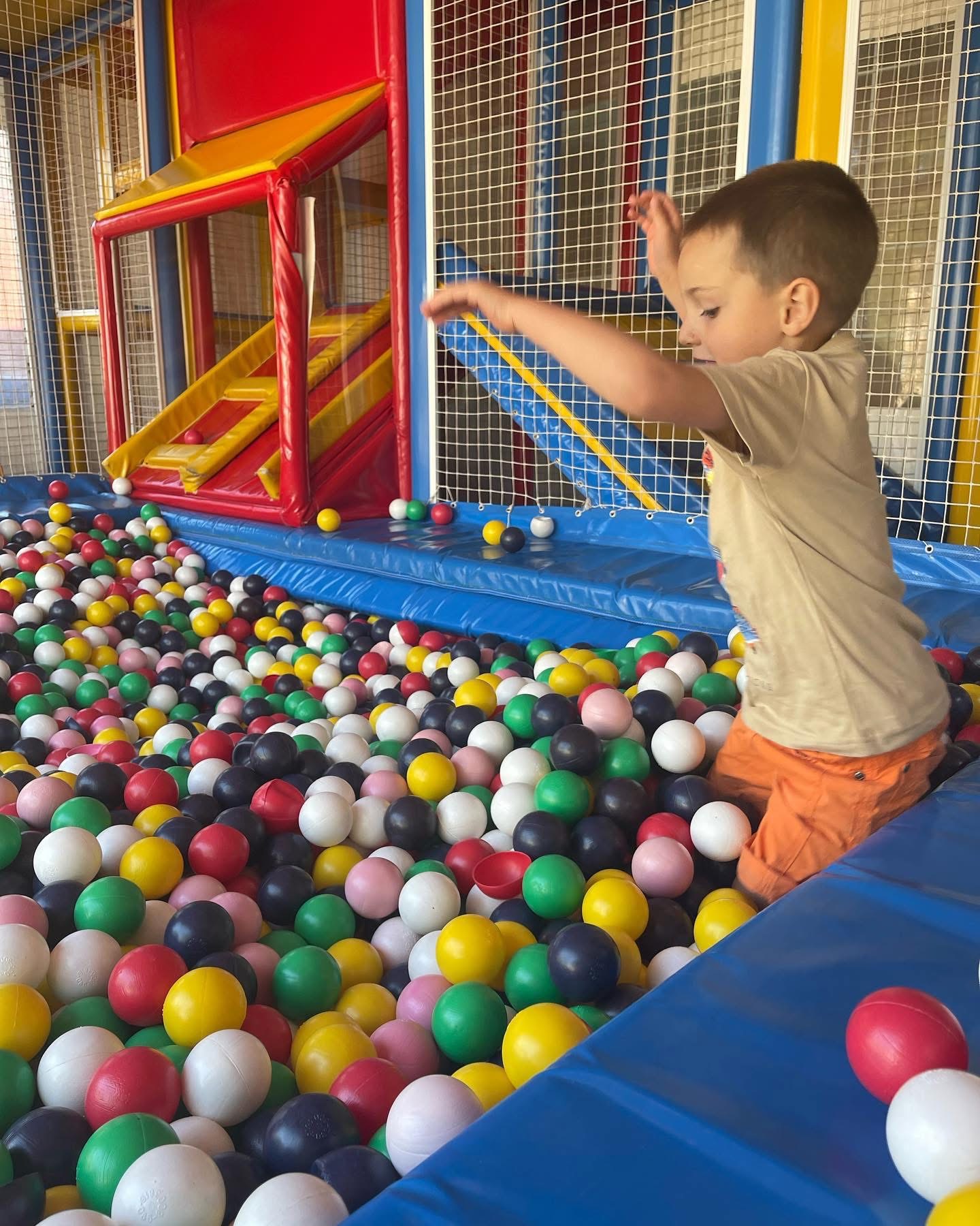 Un bambino gioca nella vasca delle palline colorate accanto allo scivolo